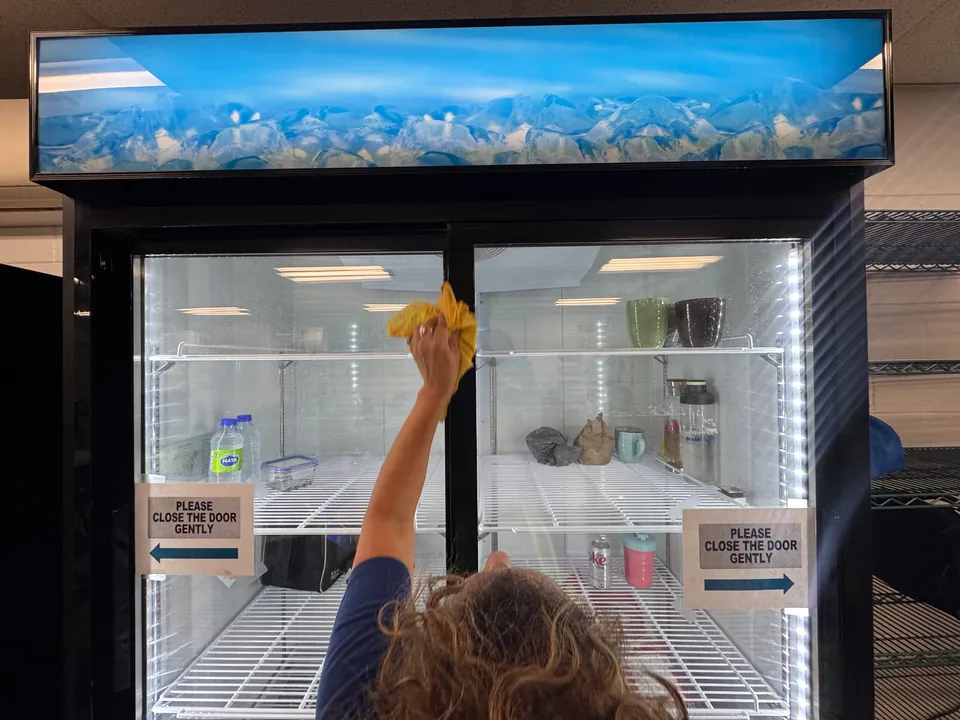 Cleaner wiping the glass doors of a commercial refrigerator